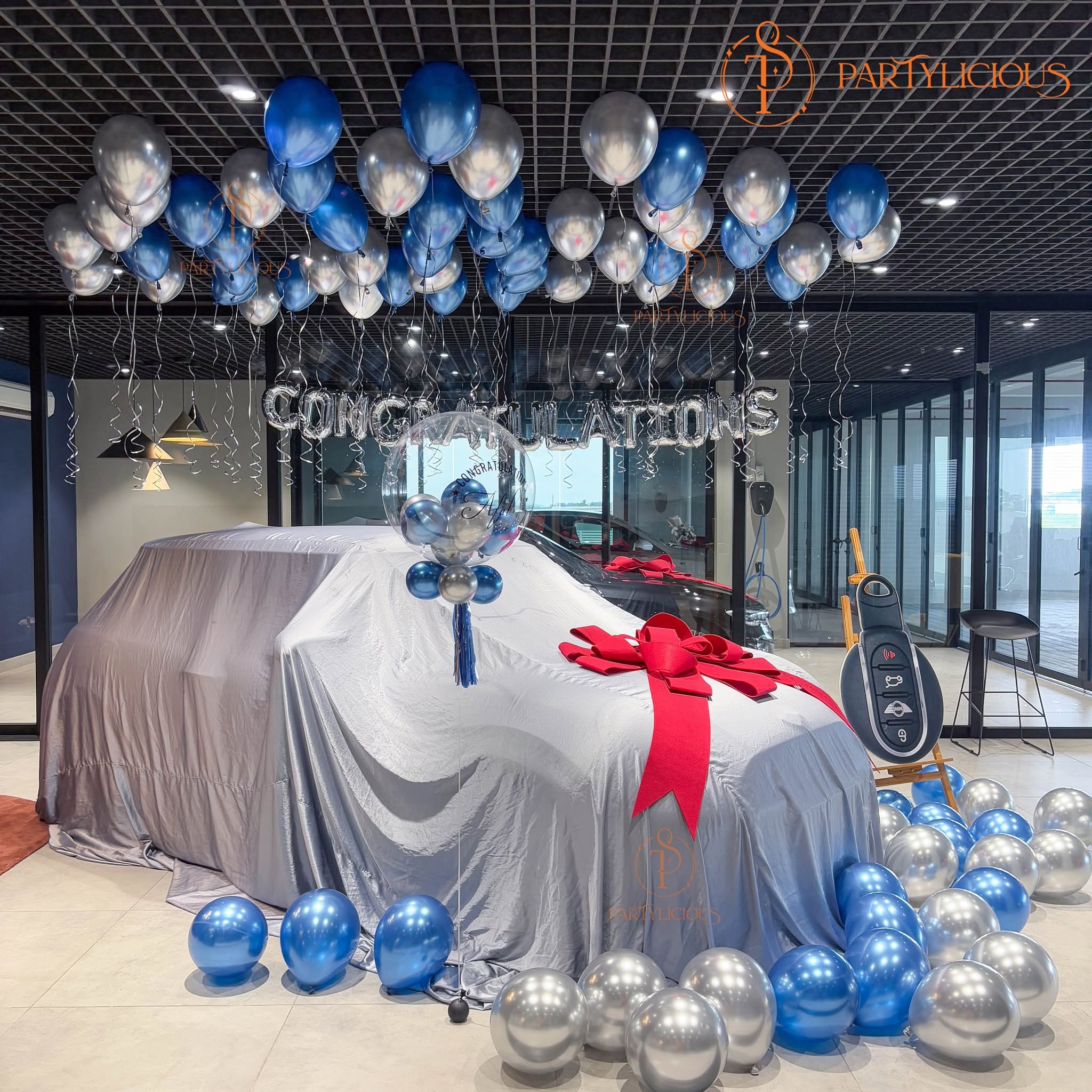 Giant car key prop on an easel next to the balloon decorated handover car