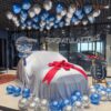 Car showroom balloon decoration with a ceiling of helium balloons and a red bow on the covered car
