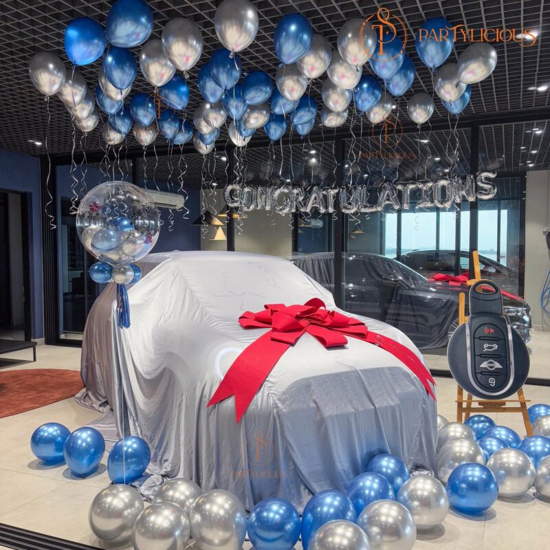 Car showroom balloon decoration with a ceiling of helium balloons and a red bow on the covered car